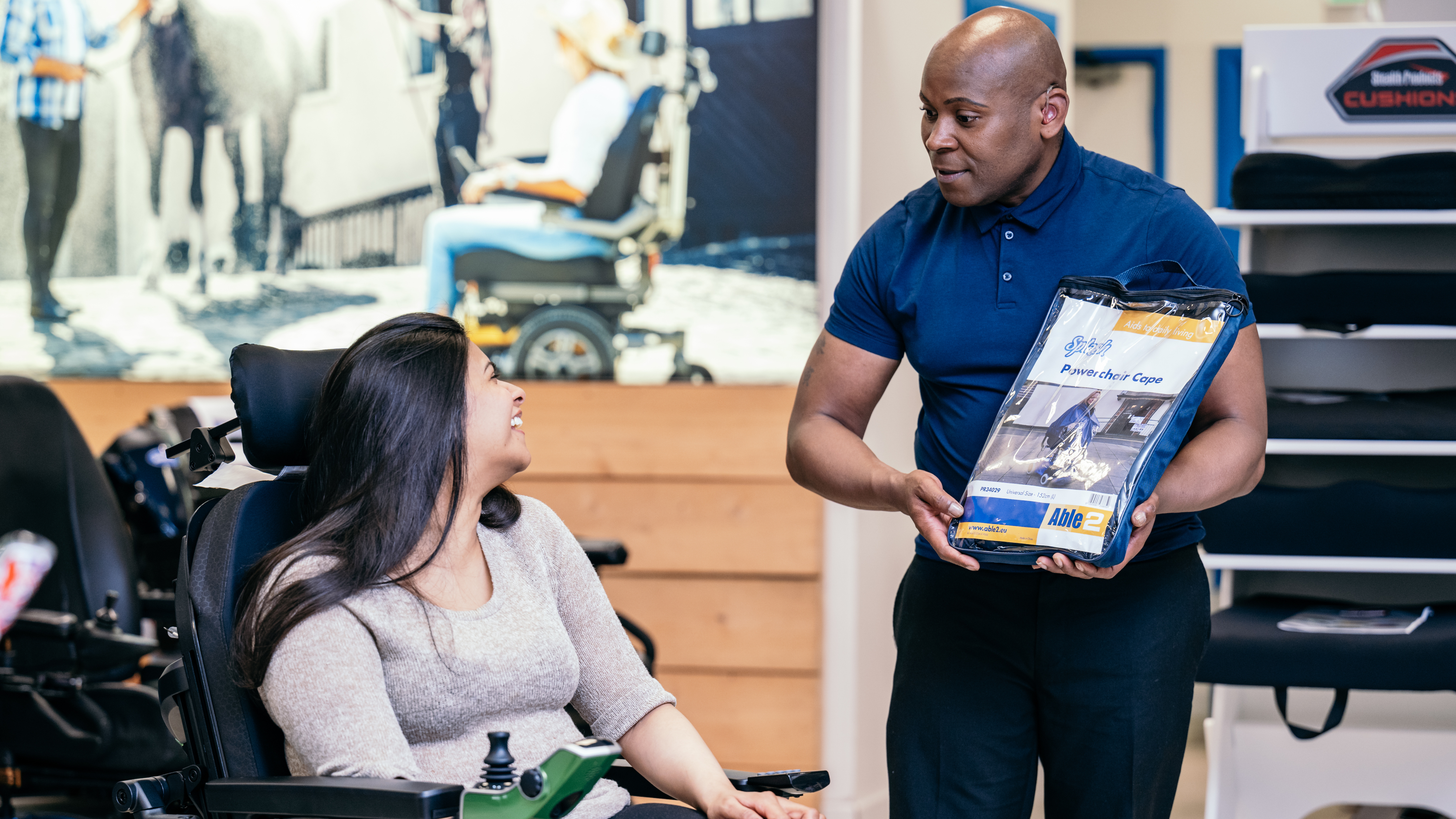 A dealer is stood presenting an information booklet to a powered wheelchair user. The powered wheelchair user is sat in their chair looking back at the dealer.