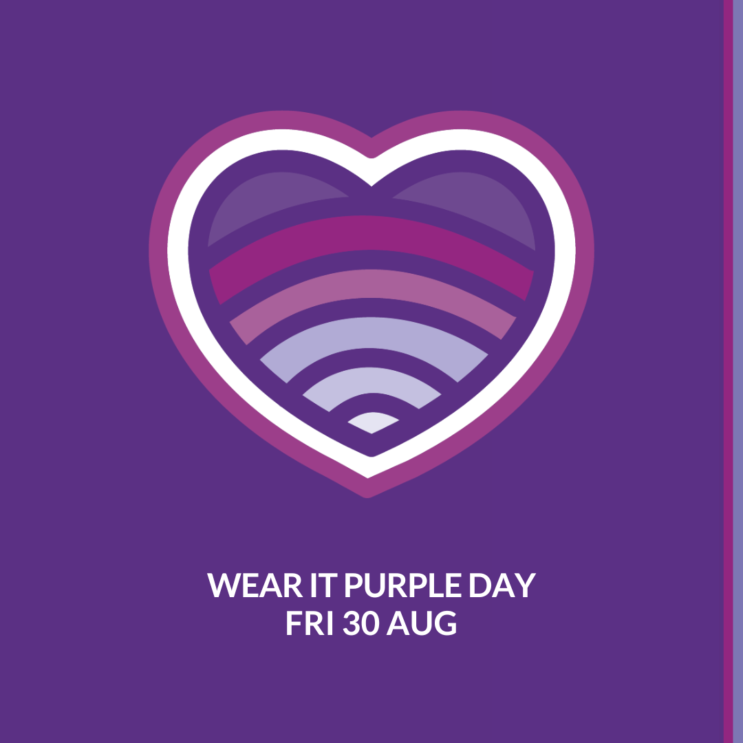 The graphic shows a purple heart with a rainbow in the middle, against a deep purple background. Below the heart sits the words â€˜JOIN US FOR WEAR IT PURPLE DAY FRI 30 AUGâ€™. 