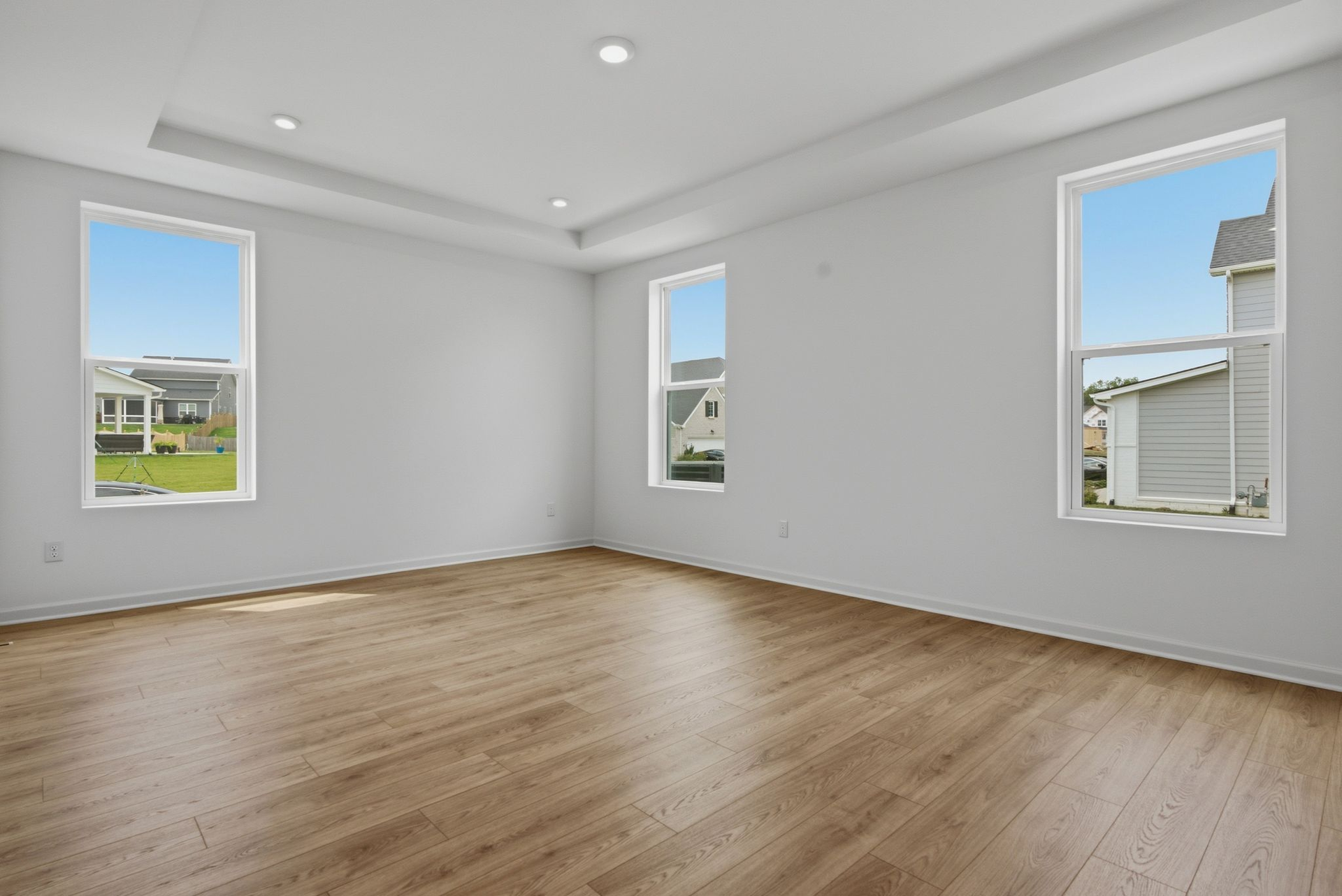 primary bedroom with wood floors, large windows, white walls, and tray ceiling