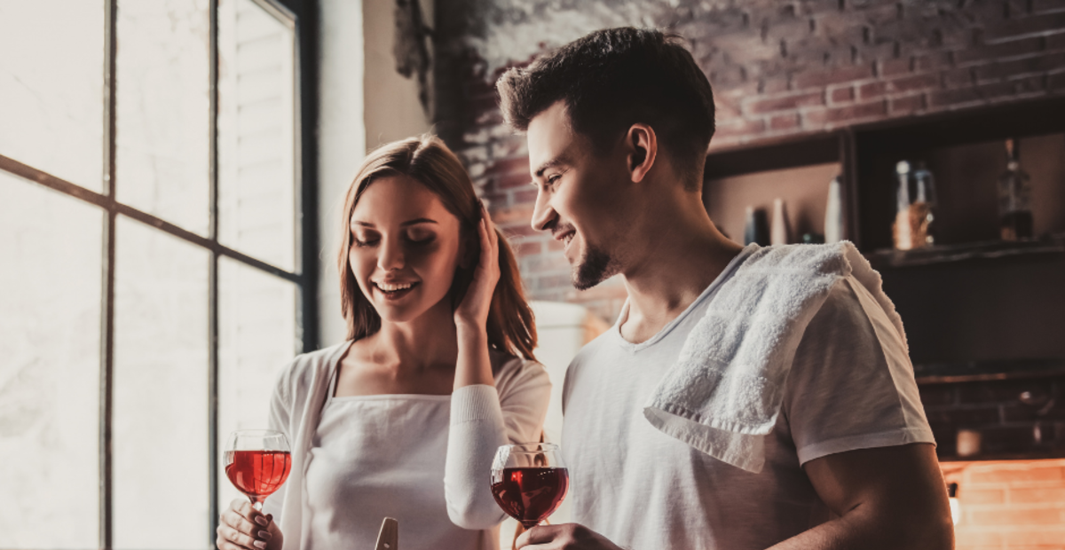 Couple cooking valentines dinner with a glass of red wine.
