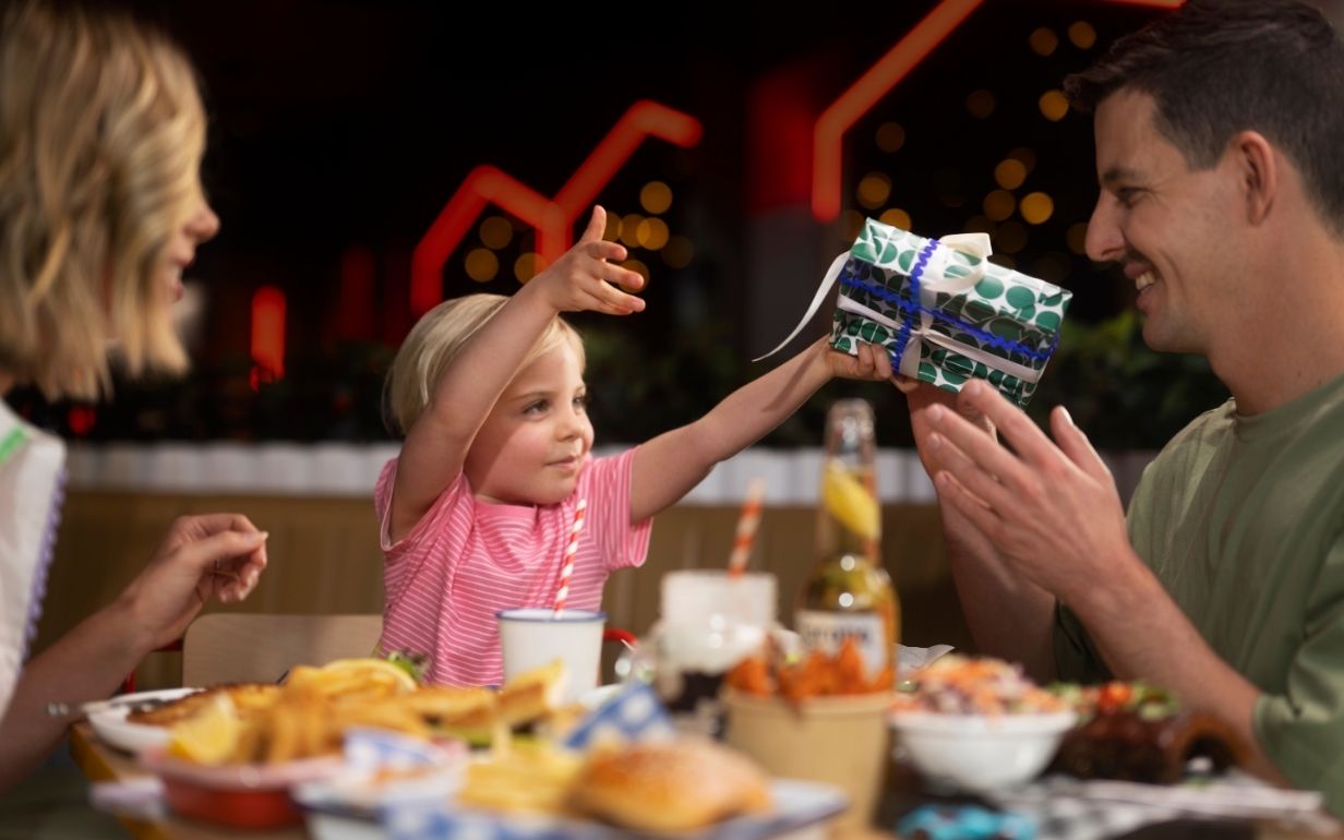 Dad receiving a wrapped Father’s Day gift from a child while sharing a meal together.