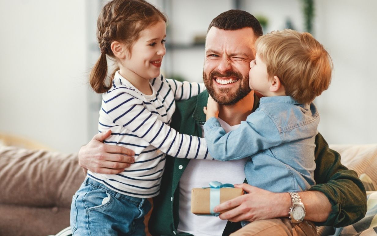 Dad sharing a hug with two children while holding a Father’s Day gift.