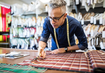 Sastre masculino con gafas cortando tela