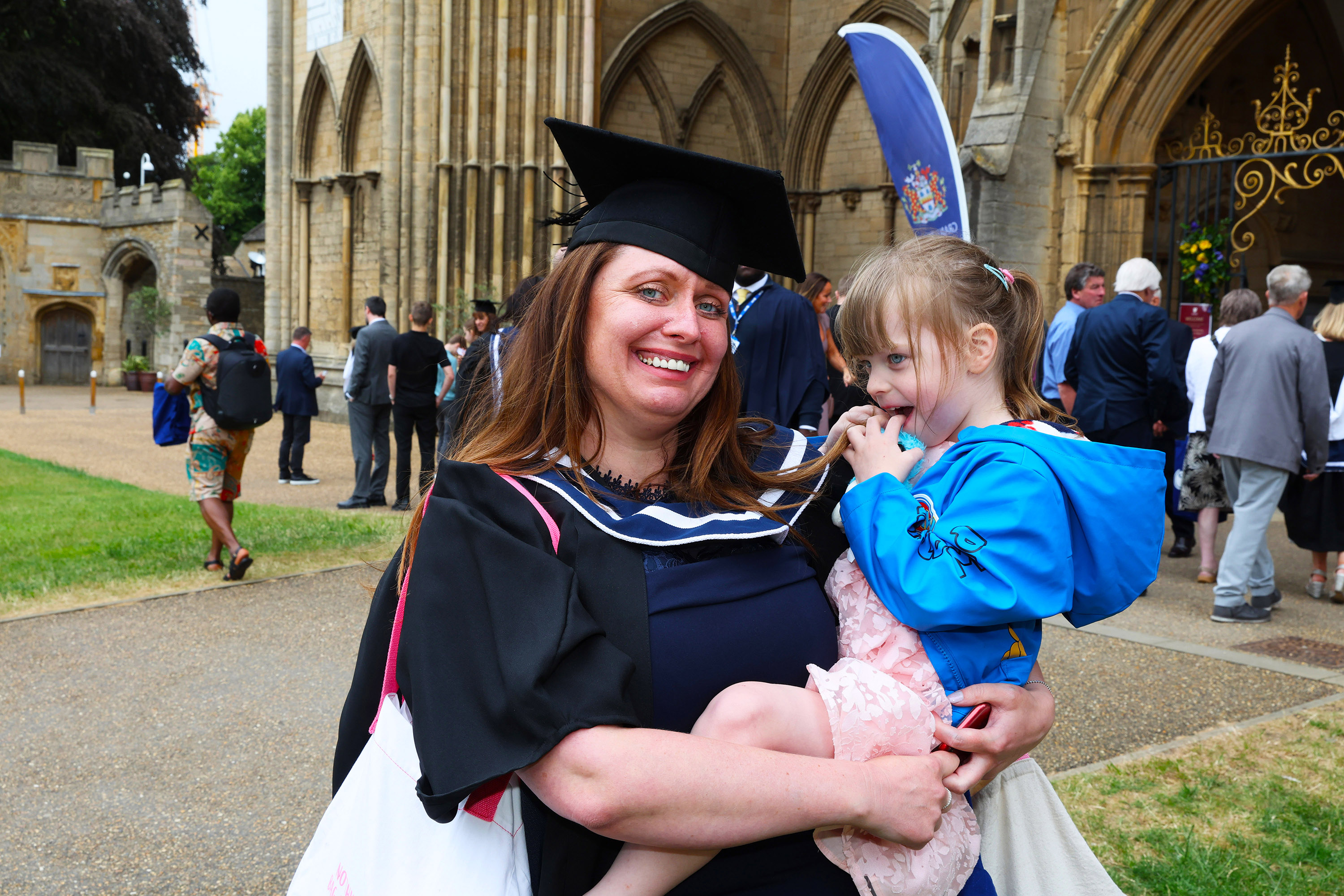 Graduate holding a young child outside the university building