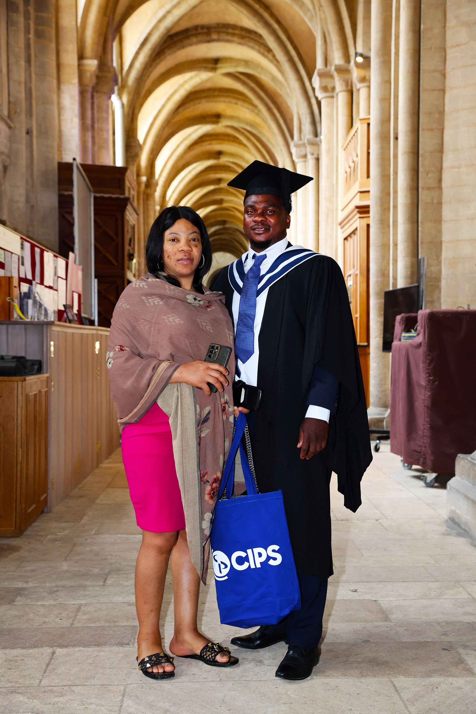 Graduate in full regalia posing with a guest in a church hallway