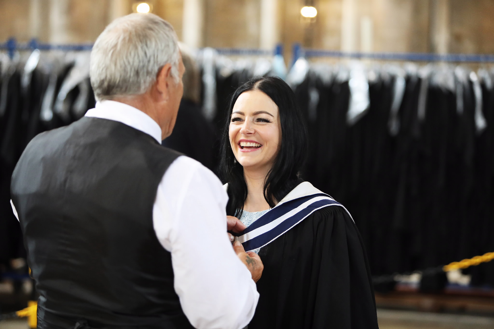 Graduate smiling while being helped with her gown or sash