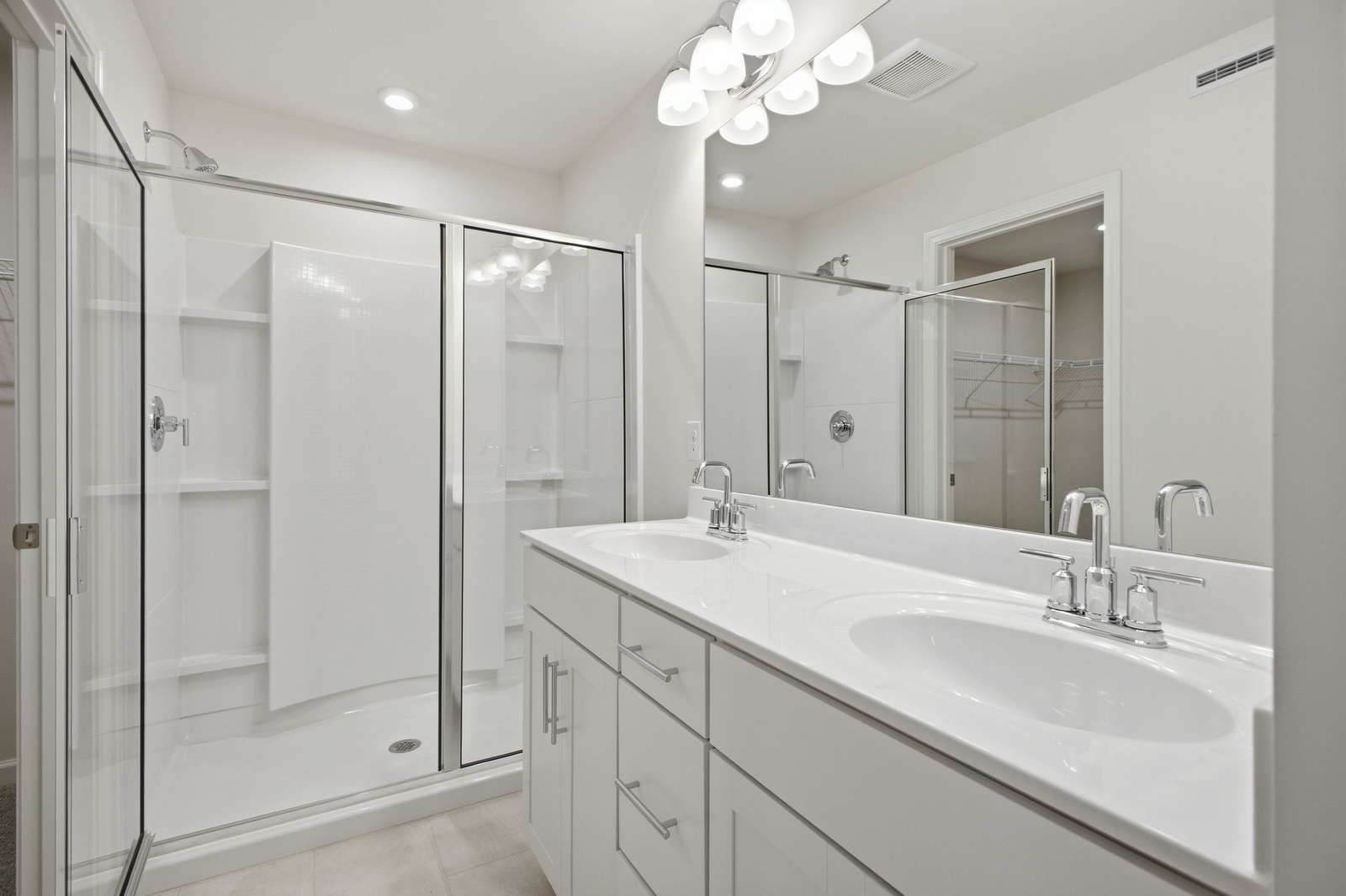 primary bathroom with oversized walk-in shower, dual sink vanity with white counter, white cabinets, and chrome hardware
