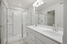 primary bathroom with oversized walk-in shower, dual sink vanity with white counter, white cabinets, and chrome hardware