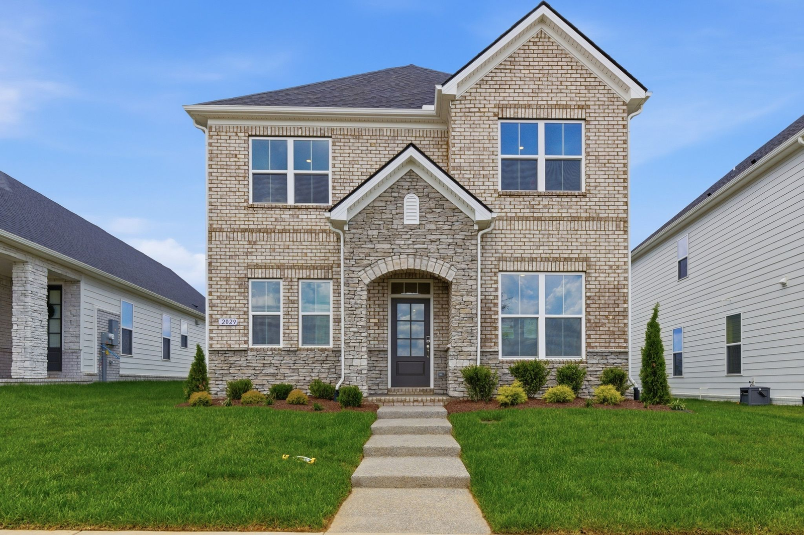 home exterior with large windows, light brown brick, a stone skirt and stone entryway with a black door