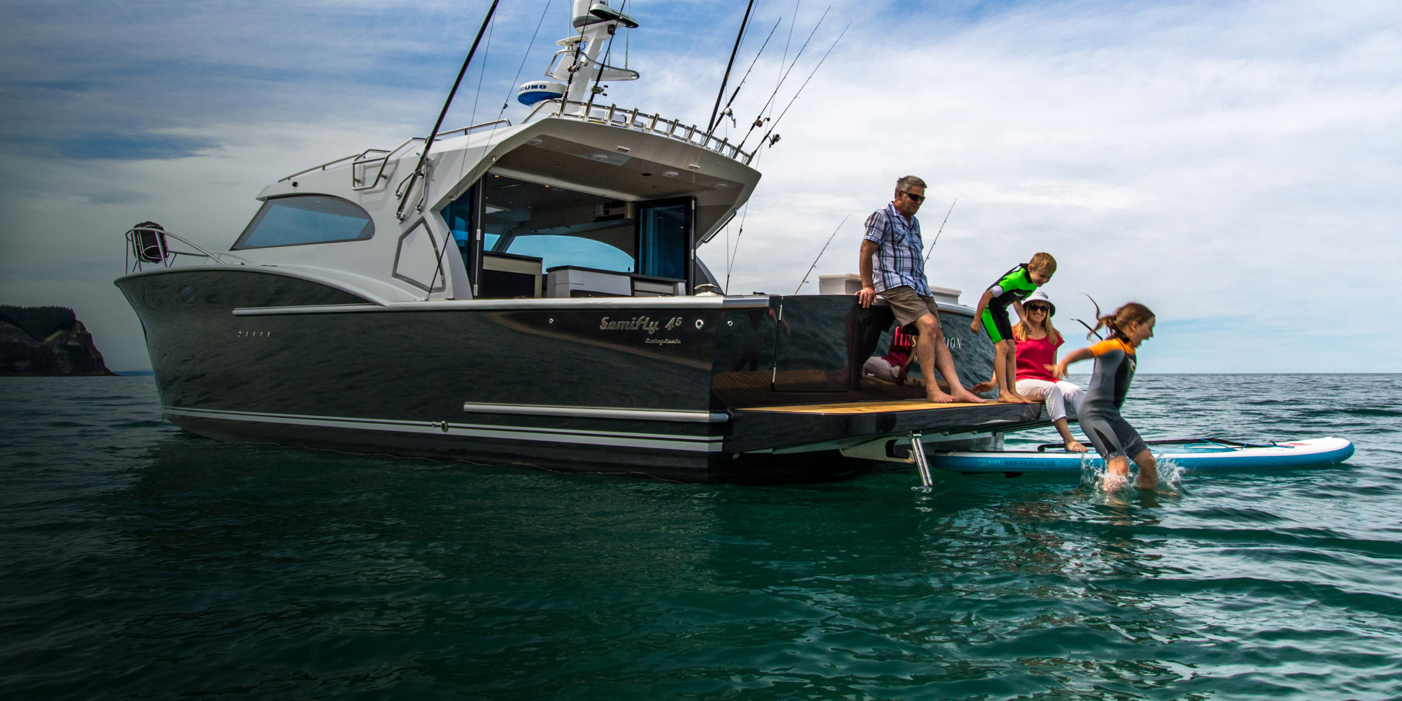 Young girl jumping into the sea from the rear platform of a powerboat as her family looks on