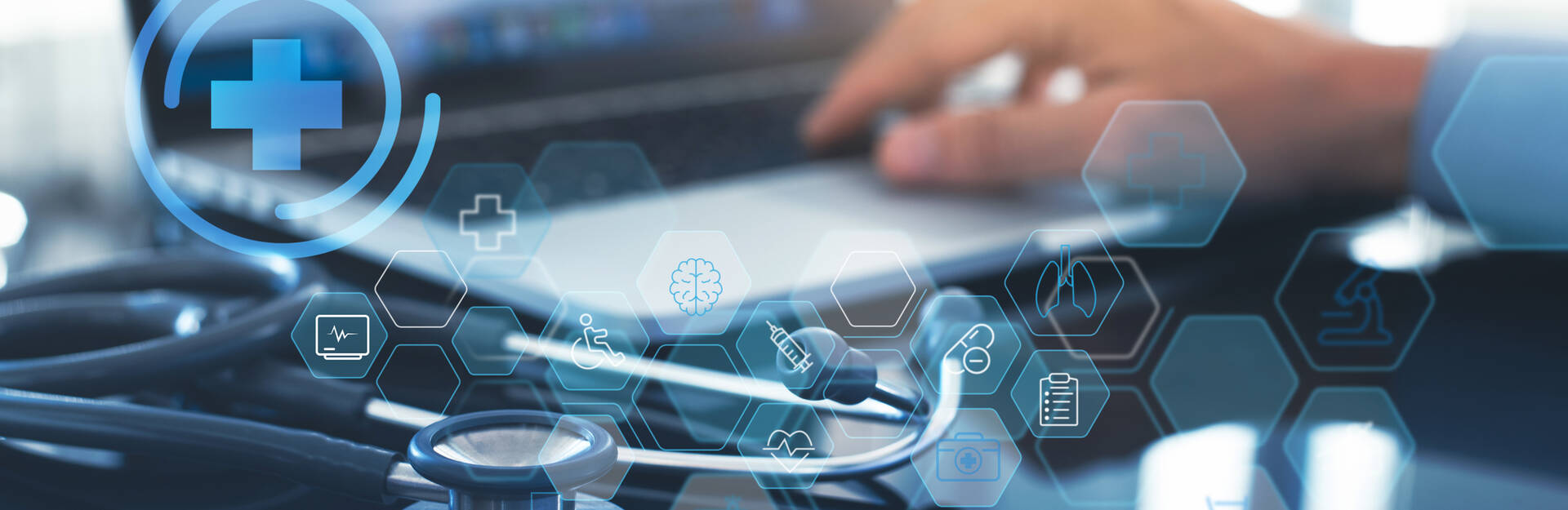 Image of a hand typing on a laptop with a stethoscope nearby. 