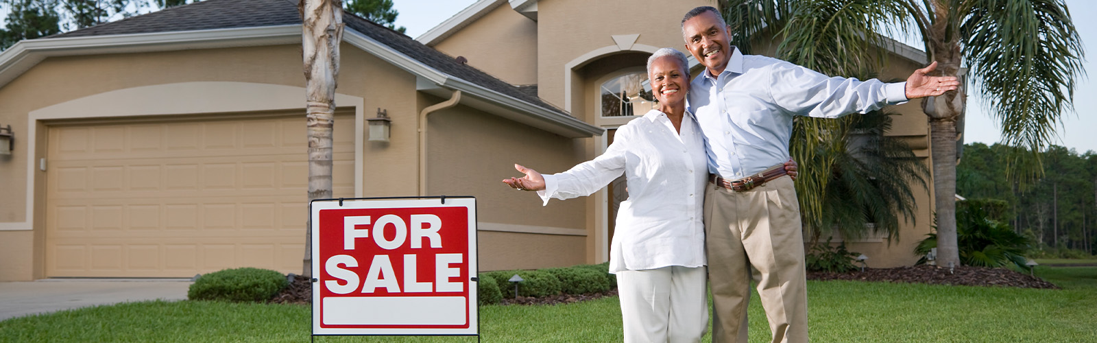 A happy couple in front a home for sale sign