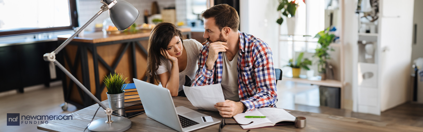 A white couple sits at a table going over paperwork in front of a laptop