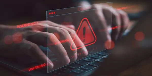 Red warning exclamation triangle over layed over image of hands typing on a laptop