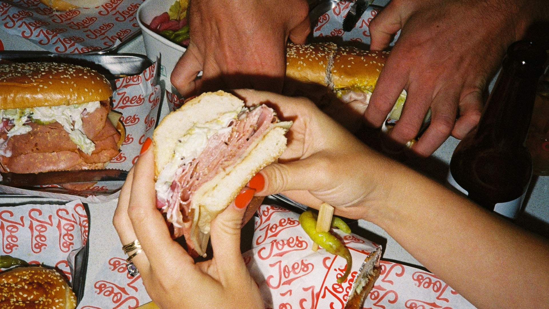 Hands holding a stacked deli sandwich filled with sliced meats, cheese and creamy dressing at Joe's Deli.