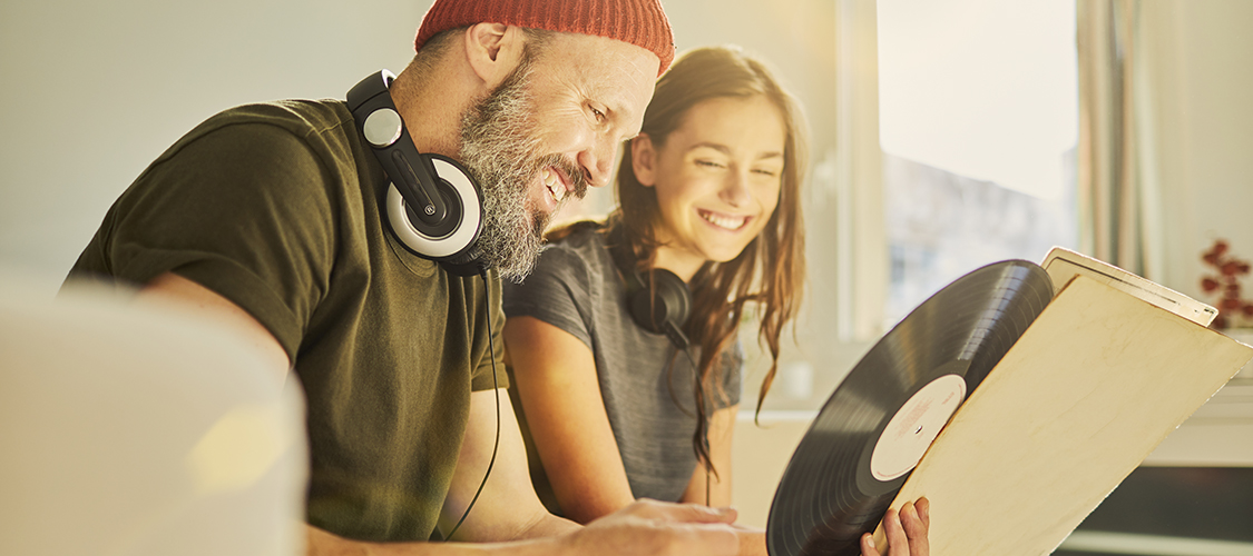 A middle-aged white man sits next to his daughter. They are both smiling while they look at records together. 