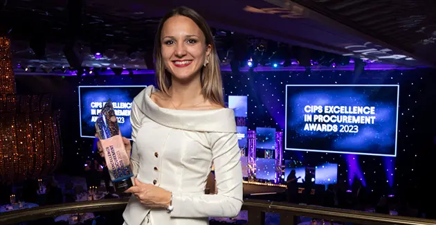 A photo of Kristina Andric holding an award infront of screens saying CIPS Excellence in procurement awards 2023