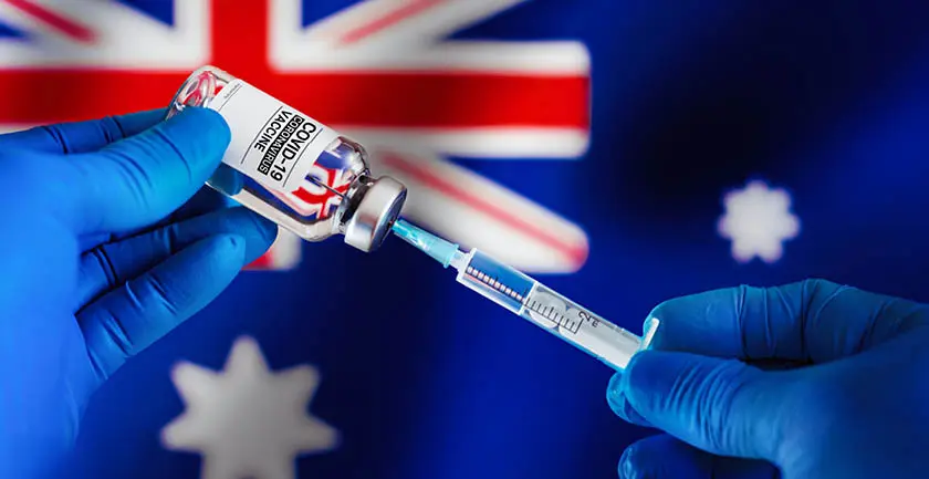 Gloved hands holding a syringe inside a COVID-19 coronovirus vaccine bottle with an Australian flag in the background 
