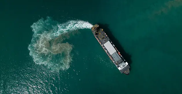 A birdseye view of a large freight ship doing a U turn on bluey green water