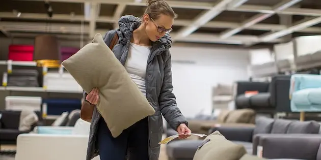 Woman in a store holding a cushion while reading a price tag.