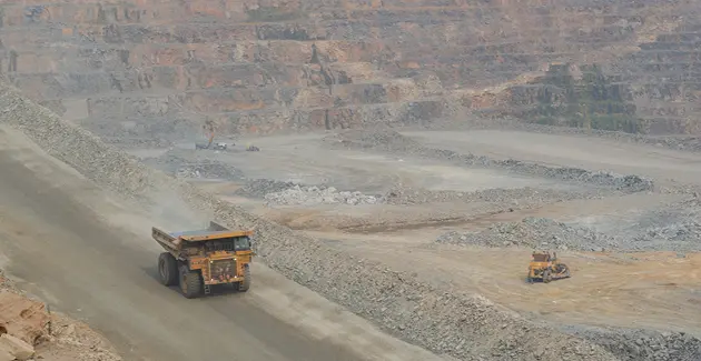 Large mining trucks operating in an open-pit mine with terraced rock walls.