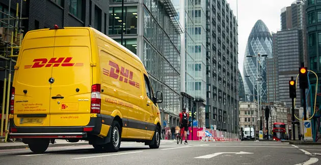 Yellow DHL van on a road in London with skyscrappers in the background