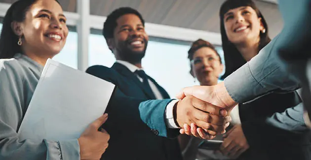 Four people facing someone off camera with his arm in shot to shake hands with a man wearing a suit