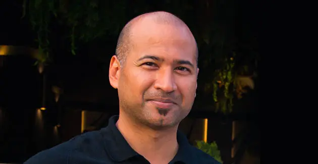 A man with a very closely shaved head is looking at the camera with kind eyes and a slight smile