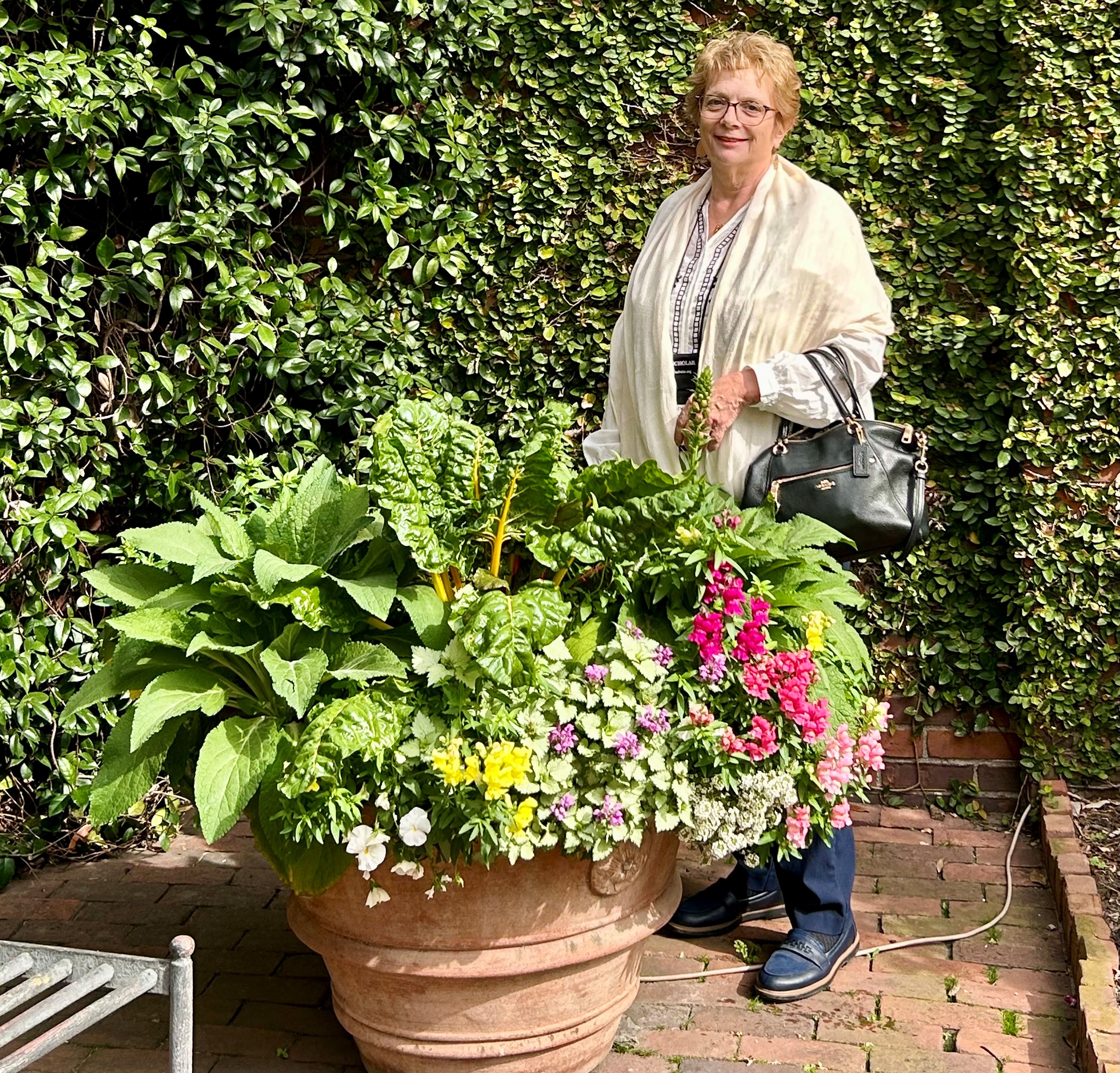 Kathryn smiles in front of hedges and flowers
