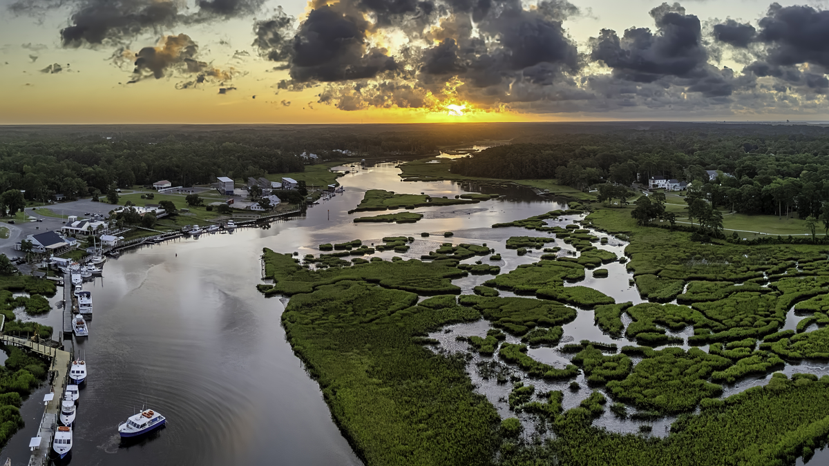 Boats on calm Little River waters at sunset over the marsh