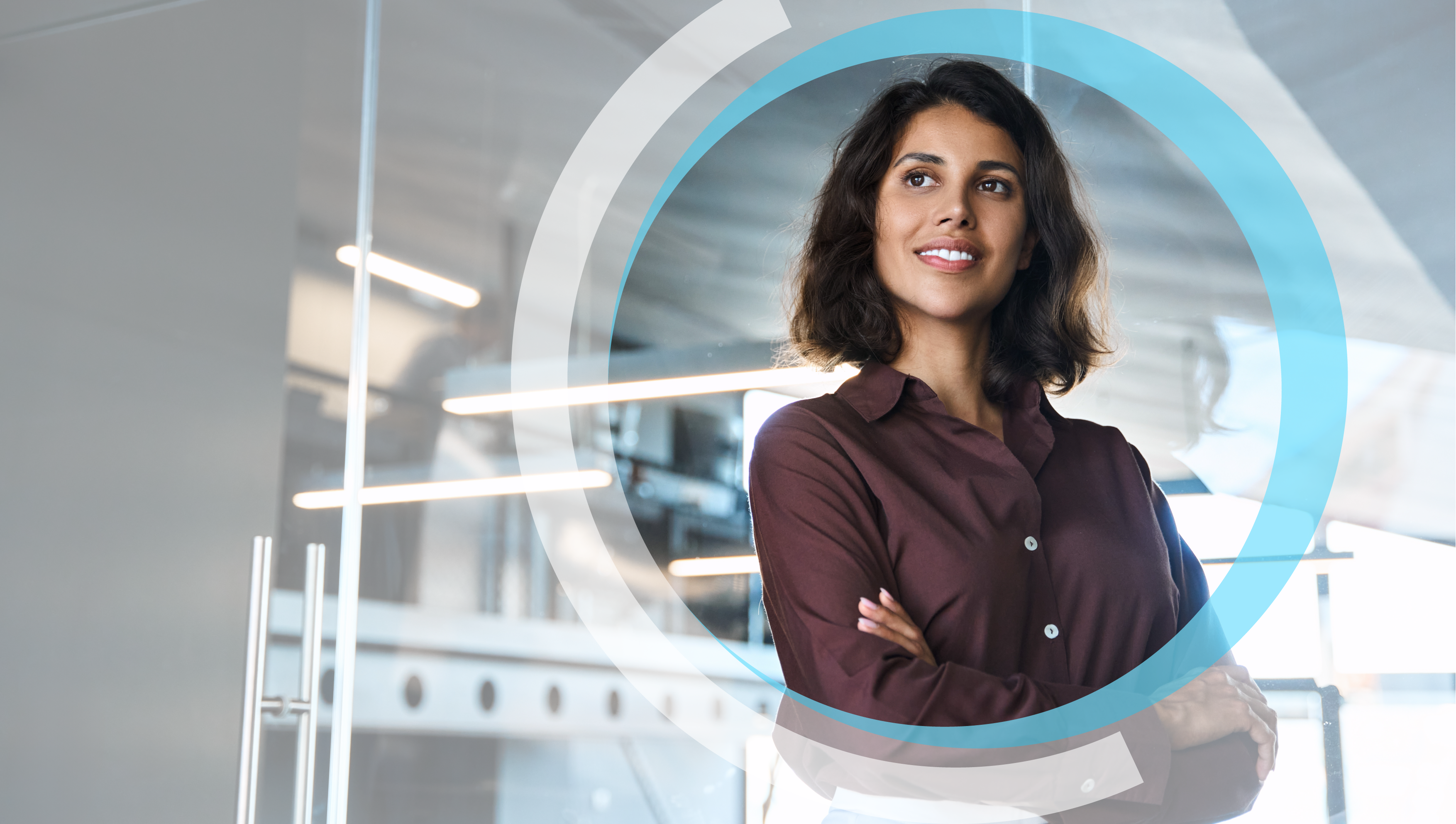 A woman stands with arms crossed in a modern office with glass walls and blurred background.