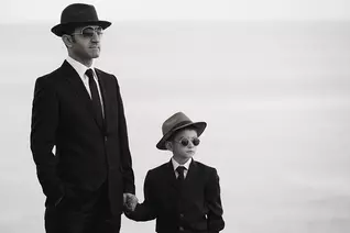 A boy holds his father's hand.