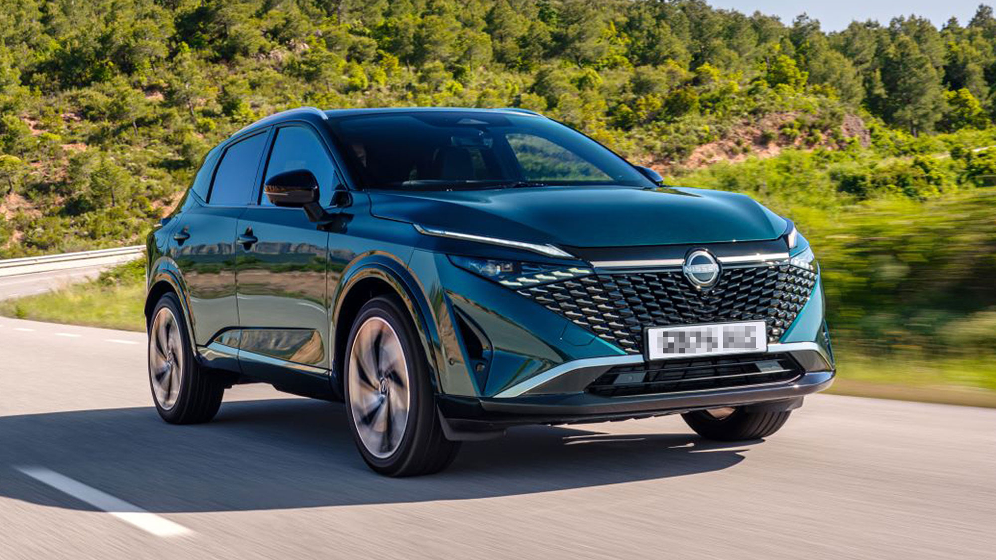 A dark green Nissan Qashqai driving on a sunny road, with a large V-motion grille and sharp, modern styling.