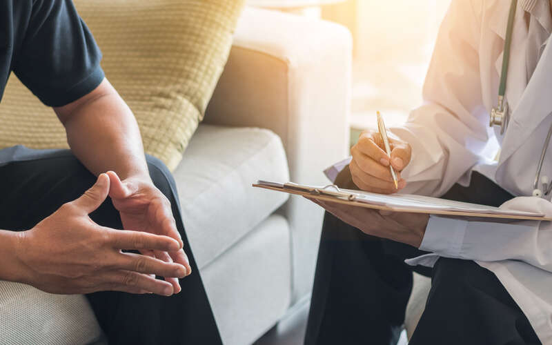 a man sitting on a couch across from a doctor holding a chart
