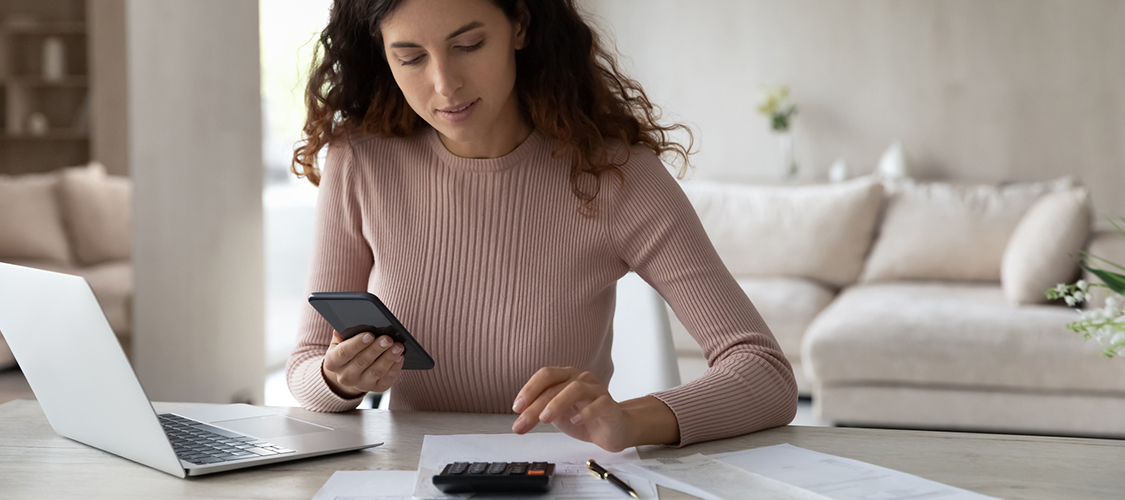 A woman sitting at a table looking at a laptop doing calculations.