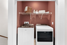 Laundry closet with a washer and dryer below a white wire shelf holding towels, baskets, and jars 