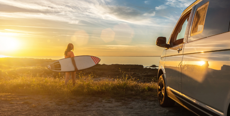 Surfer and her RV with onboard Fathom e-power system above beach at sunset