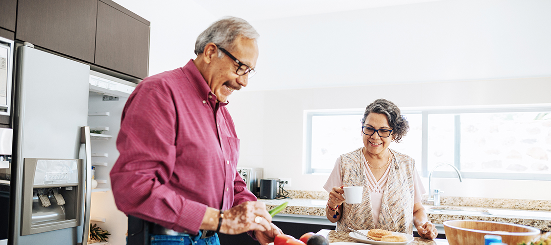 A senior Hispanic man and woman cook together in their kitchen
