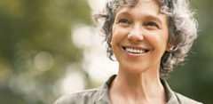 A smiling solo female traveler with short gray hair looks thoughtfully into the distance while enjoying the outdoors.