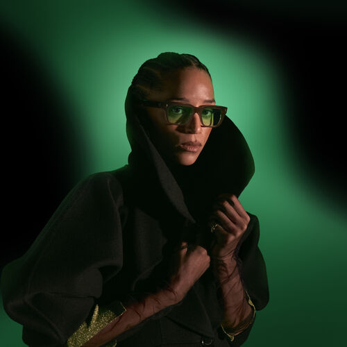 Woman with green tinted sunglasses in front of a dark green background