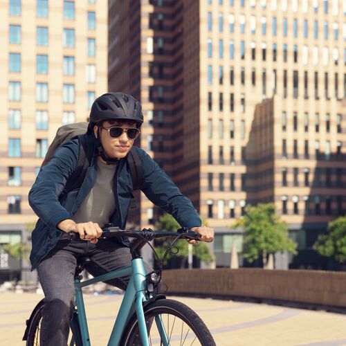 Un homme fait du VTT en ville, portant un casque et des lunettes de soleil HOYA Sensity Fast