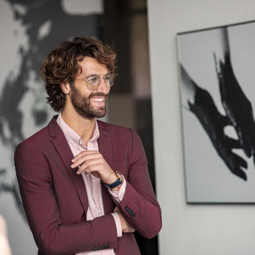 Hombre rubio con traje rojo y gafas con lentes HOYA Sensity en interiores