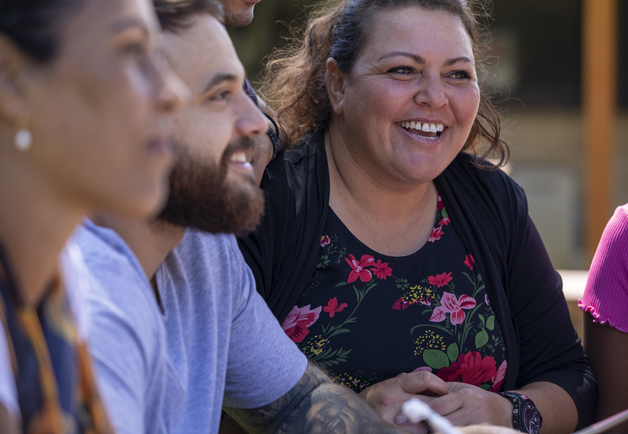 Close-up of a smiling woman in a floral dress talking with others during an outdoor group meeting.