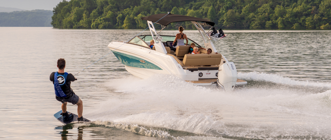 Man wakesurfing on a tranquil lake, towed by a powerboat fitted with Lenco trim tabs