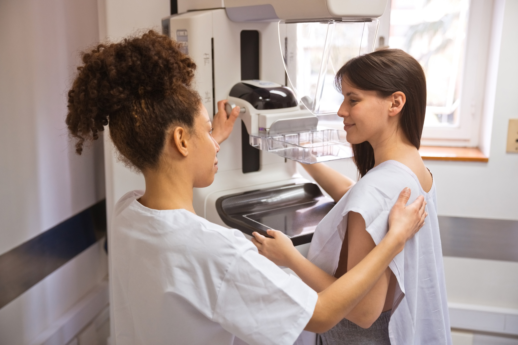 A woman talks with a nurse near mammogram equipment