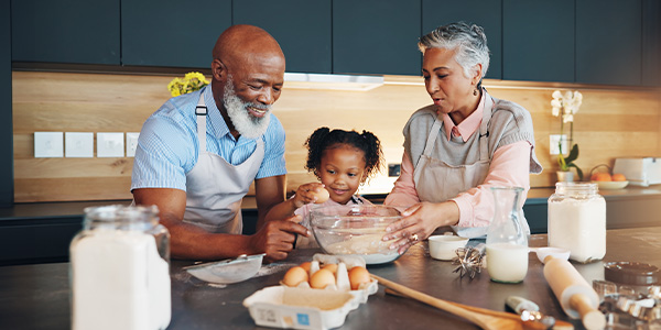 A older Black man and woman stand in a kitchen helping a young Black girl cook