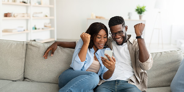 A Black couple celebrates on a couch.