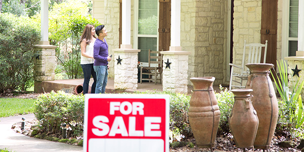 A white woman and an Asian man stand together in front of a large white stone home with a 