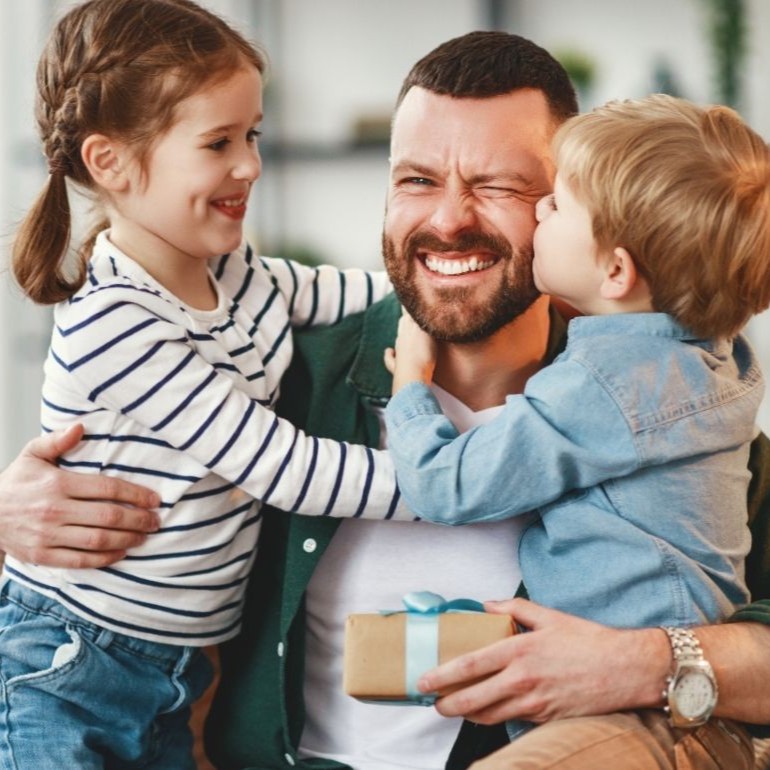 Dad sharing a hug with two children while holding a Father’s Day gift.