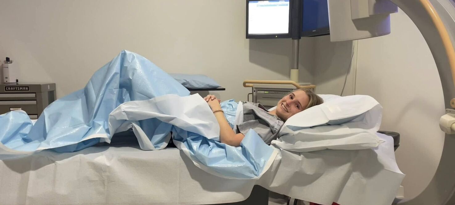 Anna Phelan lying in a hospital bed, smiling at the camera